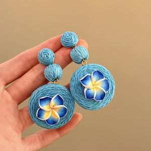 Primo piano dettagliato di orecchini pendenti in rafia blu con fiore in pasta polimerica