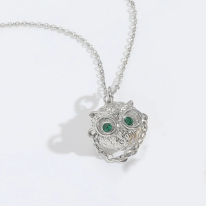 Detail of silver owl pendant with green gemstone eyes on a delicate link chain