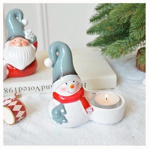Ceramic snowman candle holder with hollow hat beside small gnome on a festive table