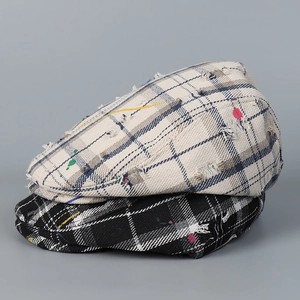 Close-up of distressed plaid flat cap with artistic paint splatter and vintage torn details
