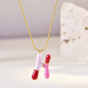 Detail of pink and red enamel letter H pendant on a golden chain necklace