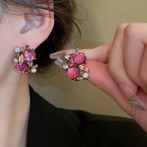 Detail view of gold-tone earrings with purple gemstones and crystals on a model