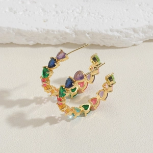 Detail of C-shaped gold hoop earrings featuring multi-colored heart-shaped zircon stones