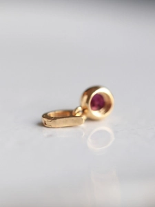 Macro shot of gold pendant featuring a pink zircon stone on white marble background