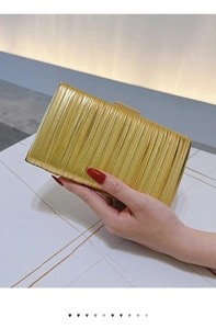 Detail of elegant gold pleated evening clutch bag held by hand for formal party events