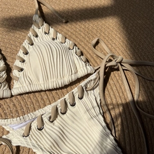 Detail of cream ribbed bikini with metallic eyelets and khaki tie strings on straw mat