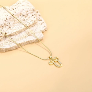 Macro detail of gold U-letter pendant with zircon stones on a snake chain necklace