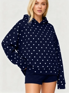 Detail view of a navy blue hoodie set with white polka dots worn by a model in soft light