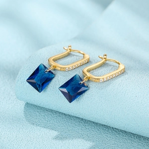 Close-up of gold U-shaped earrings with a rectangular blue gemstone and white zircons