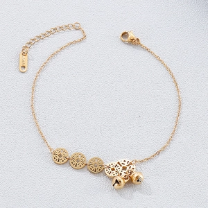 Detail of stainless steel anklet featuring hollow coins and bells on gray surface