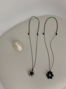 Detail of beaded flower necklaces in black and silver finishes on a neutral surface