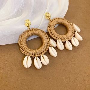 Détail de boucles d'oreilles bohèmes en raphia avec coquillages et accents dorés