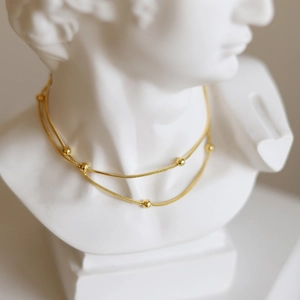 Detail of gold snake chain necklace with small beads on white plaster bust