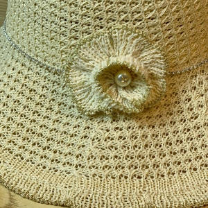 Close-up of beige woven sun hat featuring a decorative flower with pearl and silver chain