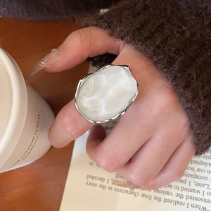 Detail of a vintage oval white resin ring with irregular silver metal setting on hand