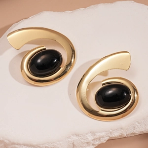 Détail de boucles d'oreilles spirales dorées avec pierre ovale noire sur pierre blanche