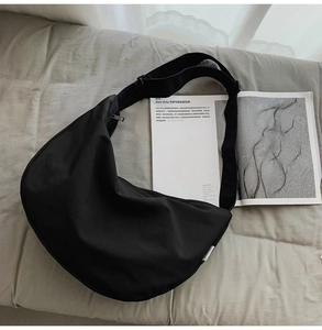 Detail of a black crescent nylon crossbody bag with wide strap on a magazine background