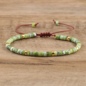Detail showing green imperial stone beads with golden spacers on a red braided bracelet