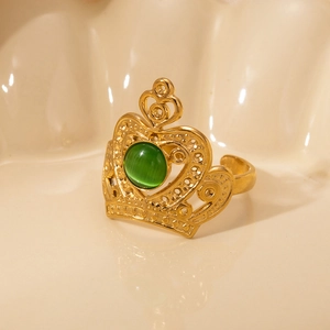 Close-up of golden crown ring with green oval gemstone in a beige shell container