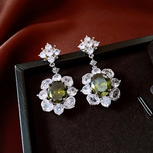 Close-up of vintage flower earrings with green stones and zircons on a dark velvet