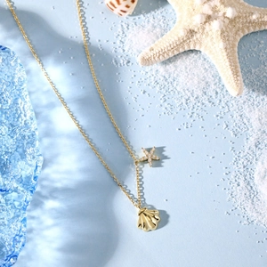 Detail of gold ocean-themed necklace with starfish pendant and shell on white sand
