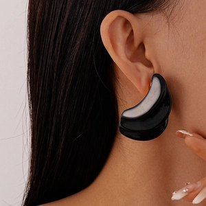 Close-up of a model wearing tiered black resin geometric wavy earrings with a glossy finish