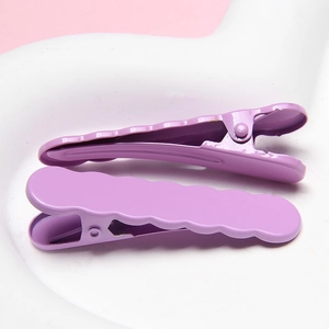 Close-up of high-quality purple metallic wavy hair clips on a white ceramic tray