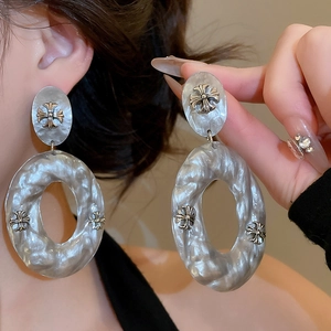 Detailed close-up of large marble texture earrings with metal cross relief design