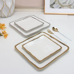 Detail view of white ceramic square plates with elegant gold and silver beaded rims