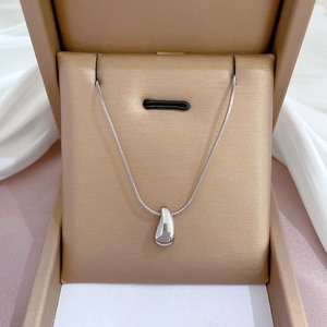 Close-up of silver teardrop pendant on snake chain inside a beige jewelry box