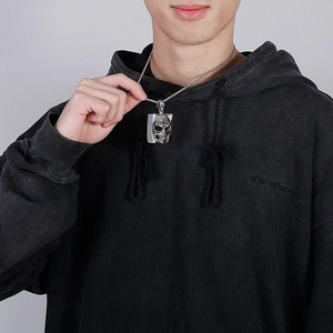 Close-up of a silver skull pendant necklace worn by a model in a black hoodie