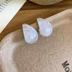 Close-up of white resin teardrop earrings with grey marble texture on a wood tray