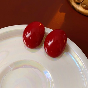 Detailed view of glossy red oval stud earrings on a pearlescent white display tray