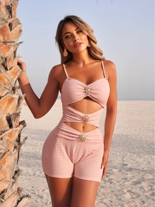 Pink textured one-piece swimsuit with golden sun buckles on a sunny beach