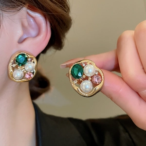 Detailed macro of vintage oval pearl earrings with green crystal and gold settings