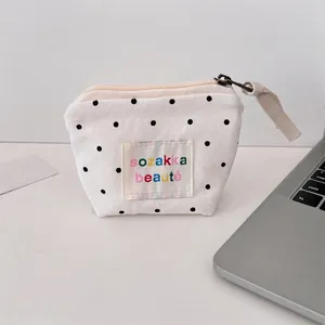 Close-up of white canvas mini makeup bag with black polka dots and zipper detail