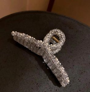 Detailed close-up of a pearl shark hair claw clip with rhinestones on a black tray