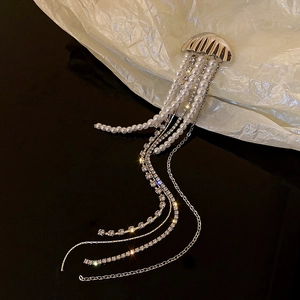 Macro shot of silver jellyfish brooch with dangling pearls and crystals on black surface