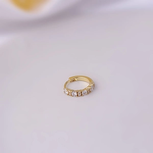Macro shot of a golden copper ear cuff with inlaid clear cubic zirconia on white cloth
