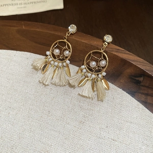 Close-up of golden dreamcatcher earrings with white pearls and soft tassels on linen background