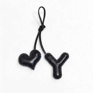 Dettaglio charm per borsa in pelle nera a forma di cuore e lettera Y con cuciture a mano