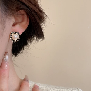 Detailed close-up of a heart-shaped pearl earring with black trim on a model's ear