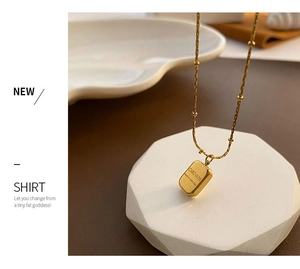 Detailed view of a gold square pendant with CHARM engraving on a white display stand