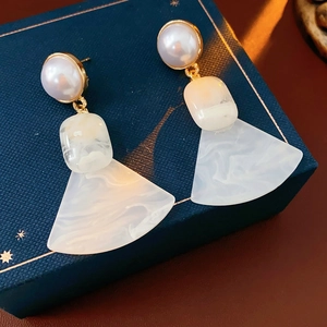 Detailed close-up of geometric fan-shaped pearl pendant earrings in a navy blue jewelry box