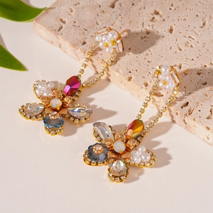 Detail of floral earrings with white pearls, colored rhinestones and golden chains