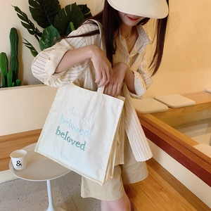 Détail de la broderie beloved sur un sac cabas en toile blanc cassé avec accents bleus