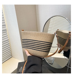 Detail of woven straw bucket bag with black stripes and brown leather strap