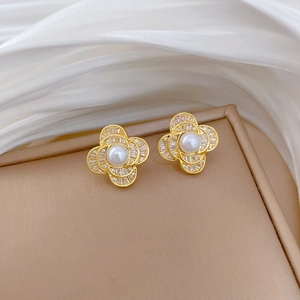 Close-up of golden clover stud earrings with white pearl and diamonds in a beige box