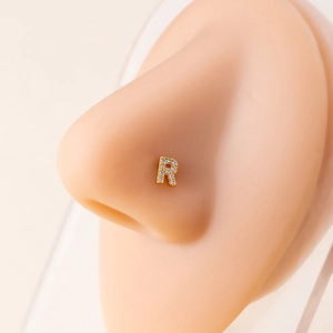 Close-up of golden letter R nose stud with micro-set zircons on a realistic silicone model