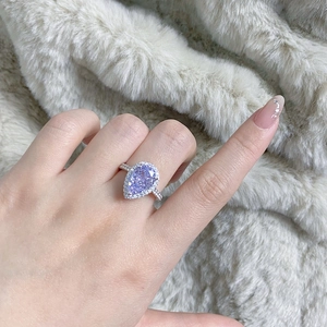 Close-up of pear-shaped lavender gemstone ring with halo design on soft beige fur background